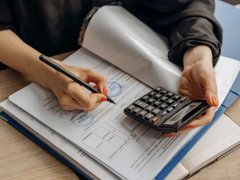 Person reviewing paperwork with a calculator and pen