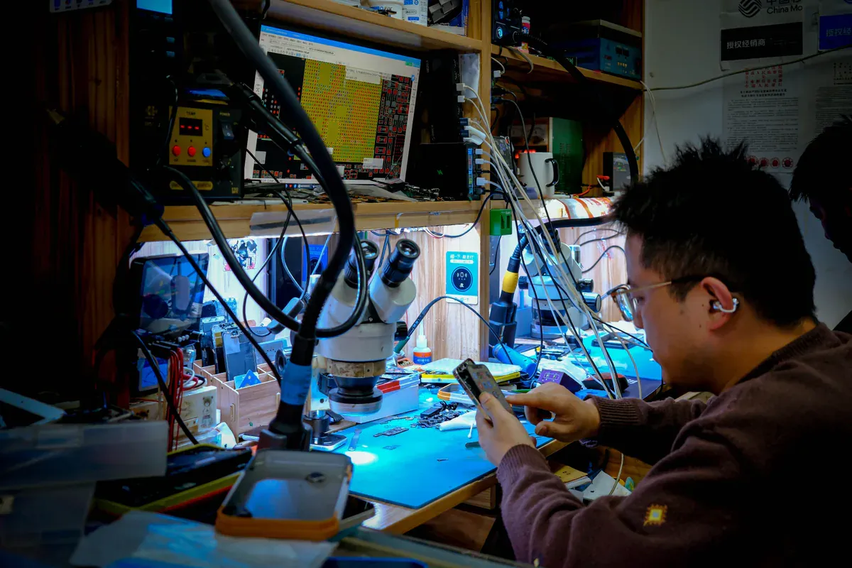 Electronics technician inspecting a populated circuit board through a bench microscope