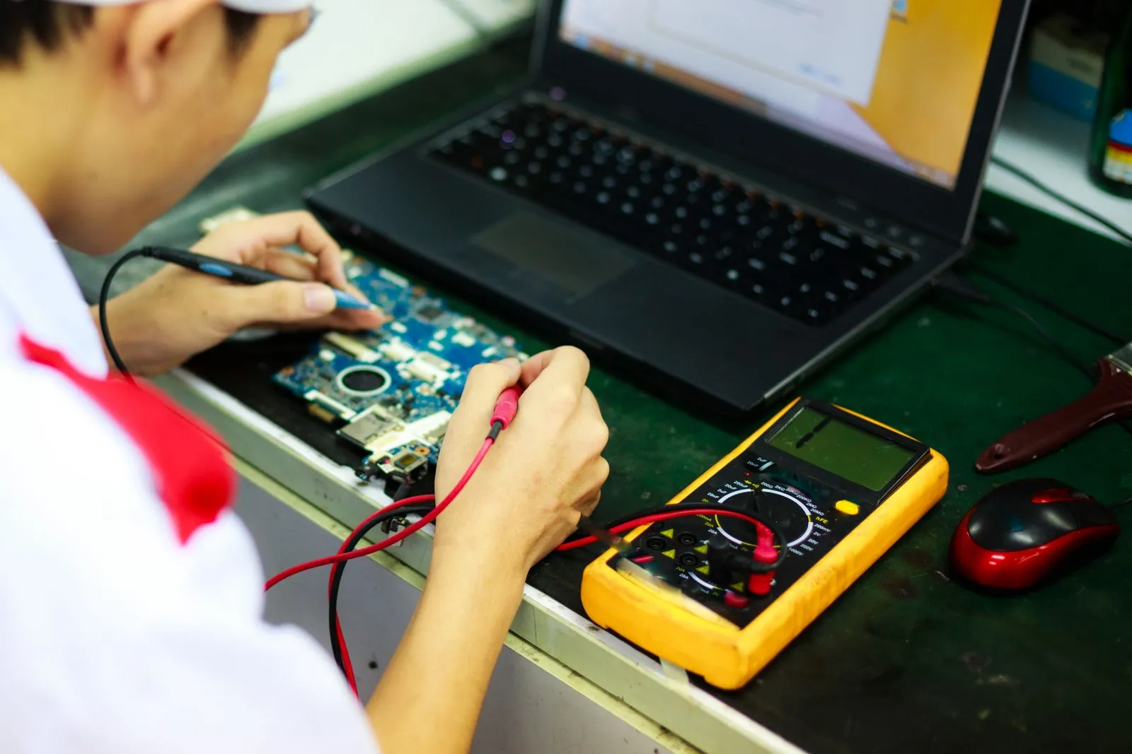 Technician recording multimeter measurements while testing a circuit board