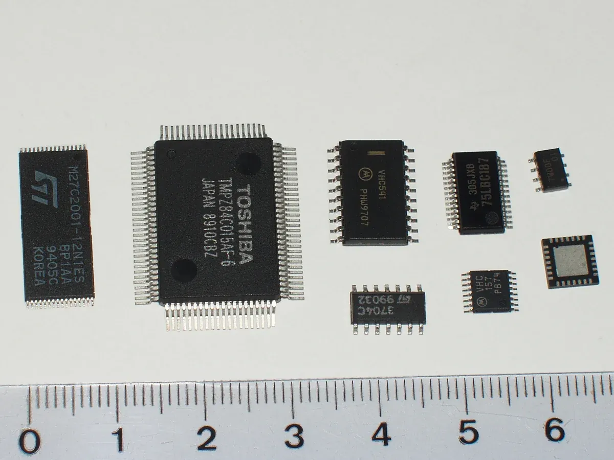 Several IC packages beside a ruler, including a QFN underside with a central exposed pad