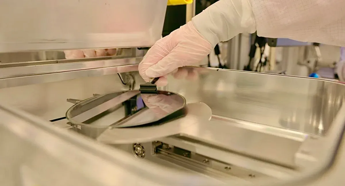 A gloved operator handles a semiconductor wafer inside processing equipment