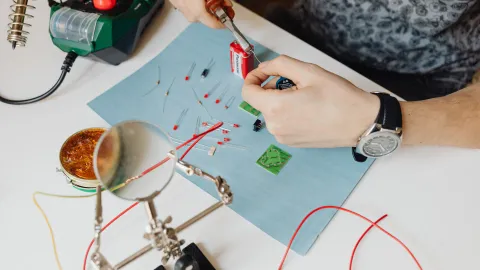 Electronics technician repairing a populated circuit board at a workbench