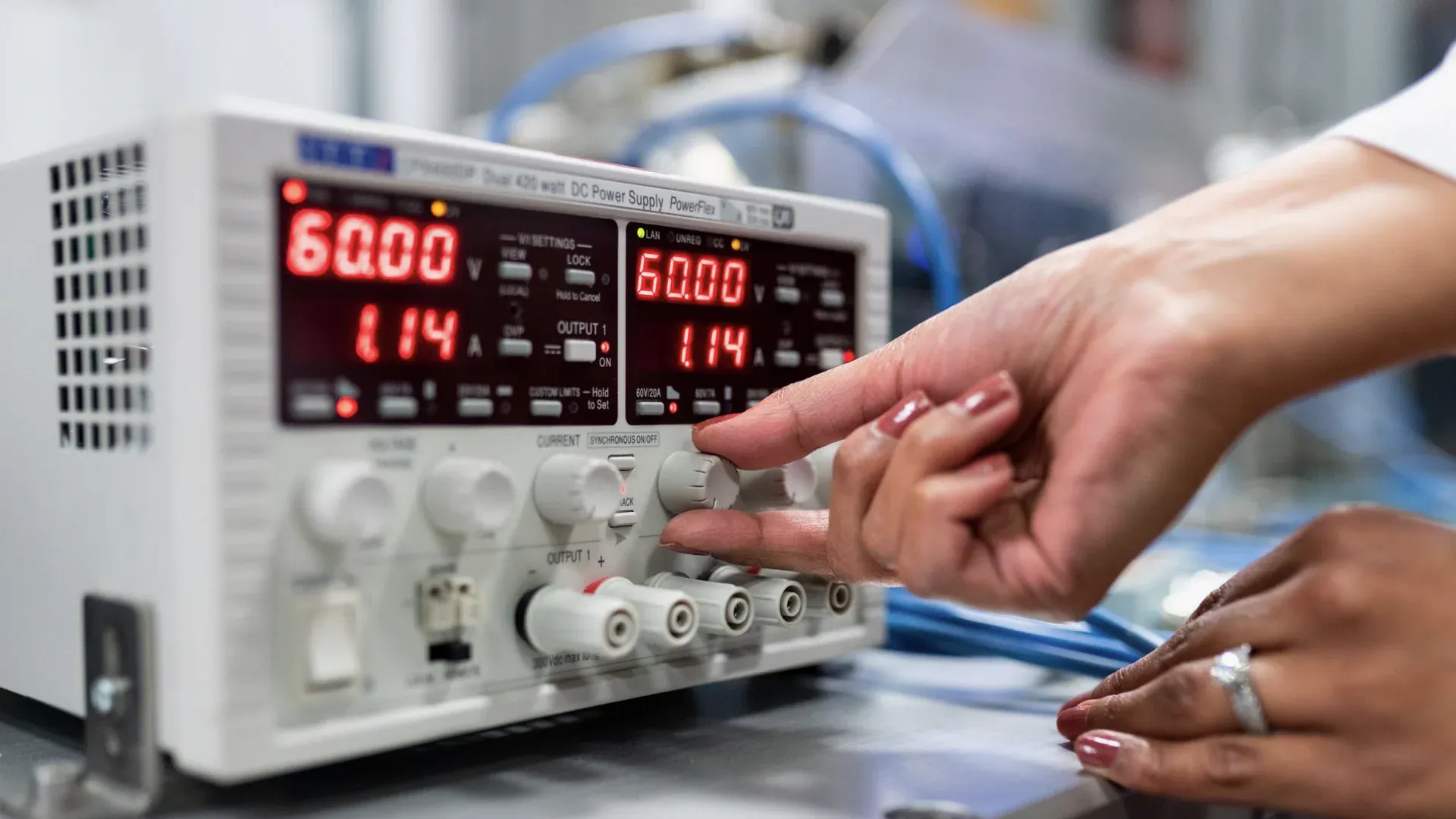 Hands adjusting a laboratory DC power supply during regulated-power measurement