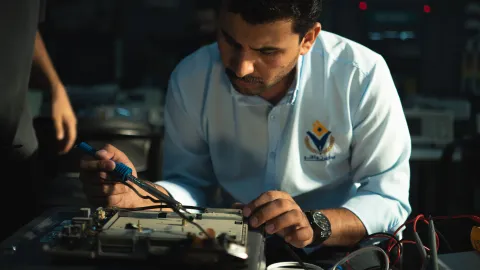 Electronics technician soldering a populated embedded control board at a workbench