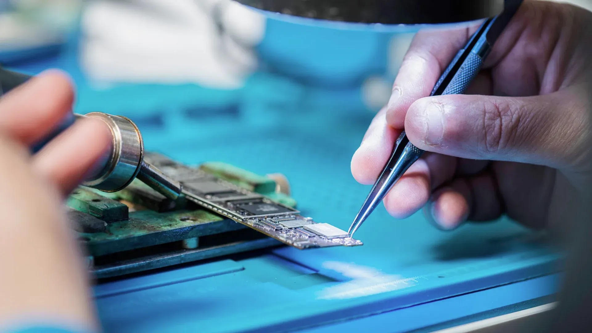 Hands inspecting and repairing a circuit board with precision tools during an electronics quality review